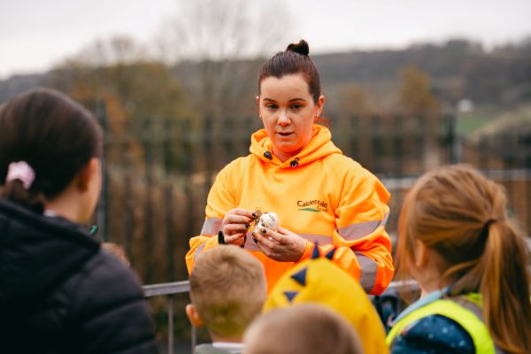 A Calderdale Council Highways team member holding an allium bulb in front of a small group of children